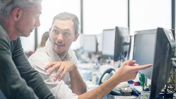 Two men in an office discuss screen recording options while gesturing to a computer screen